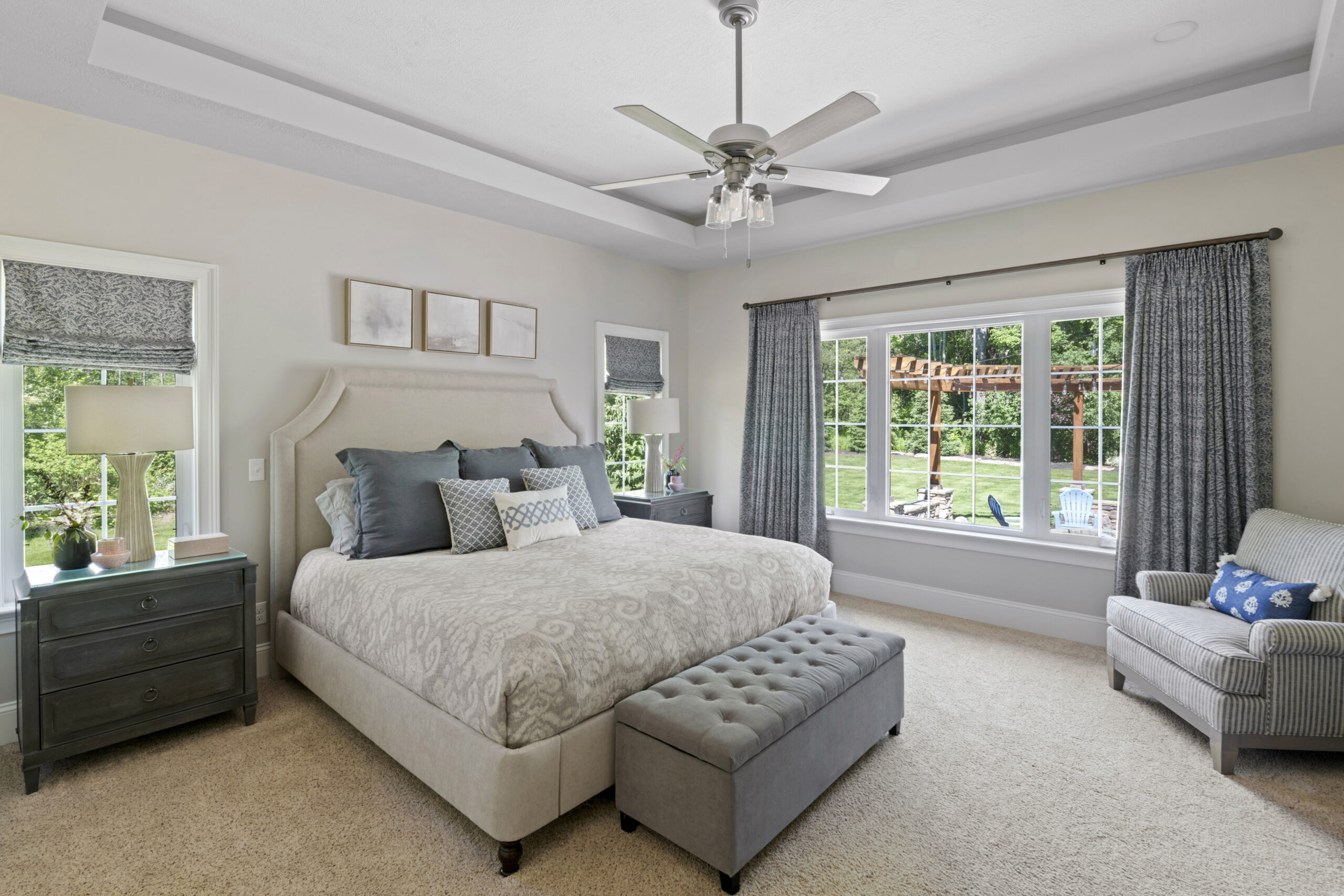 View of bedroom with grayish blue accent colors within bedding, nightstands, and curtains.