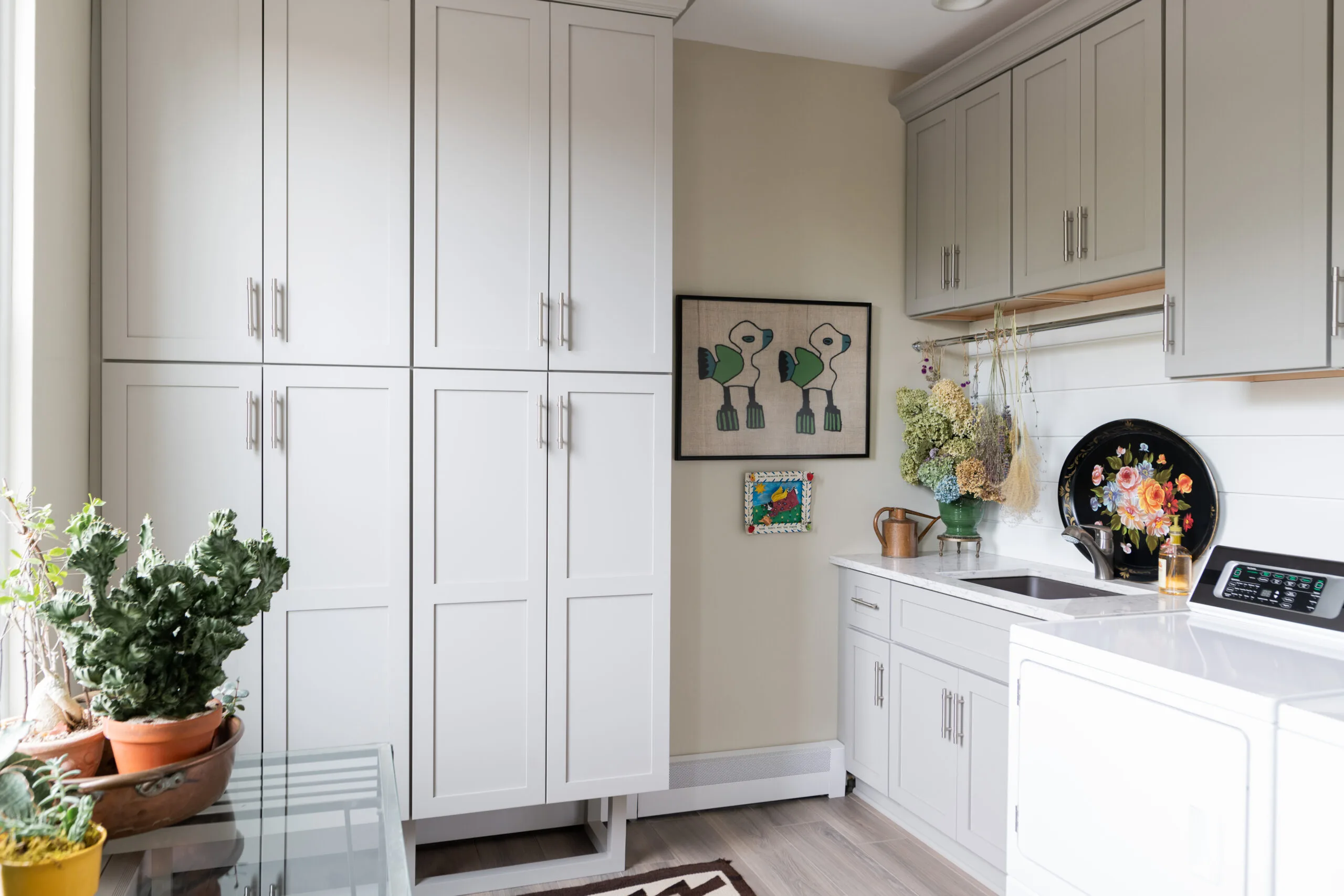 laurndy room with floor to ceiling storage cabinetry, dried flowers and quirky artwork