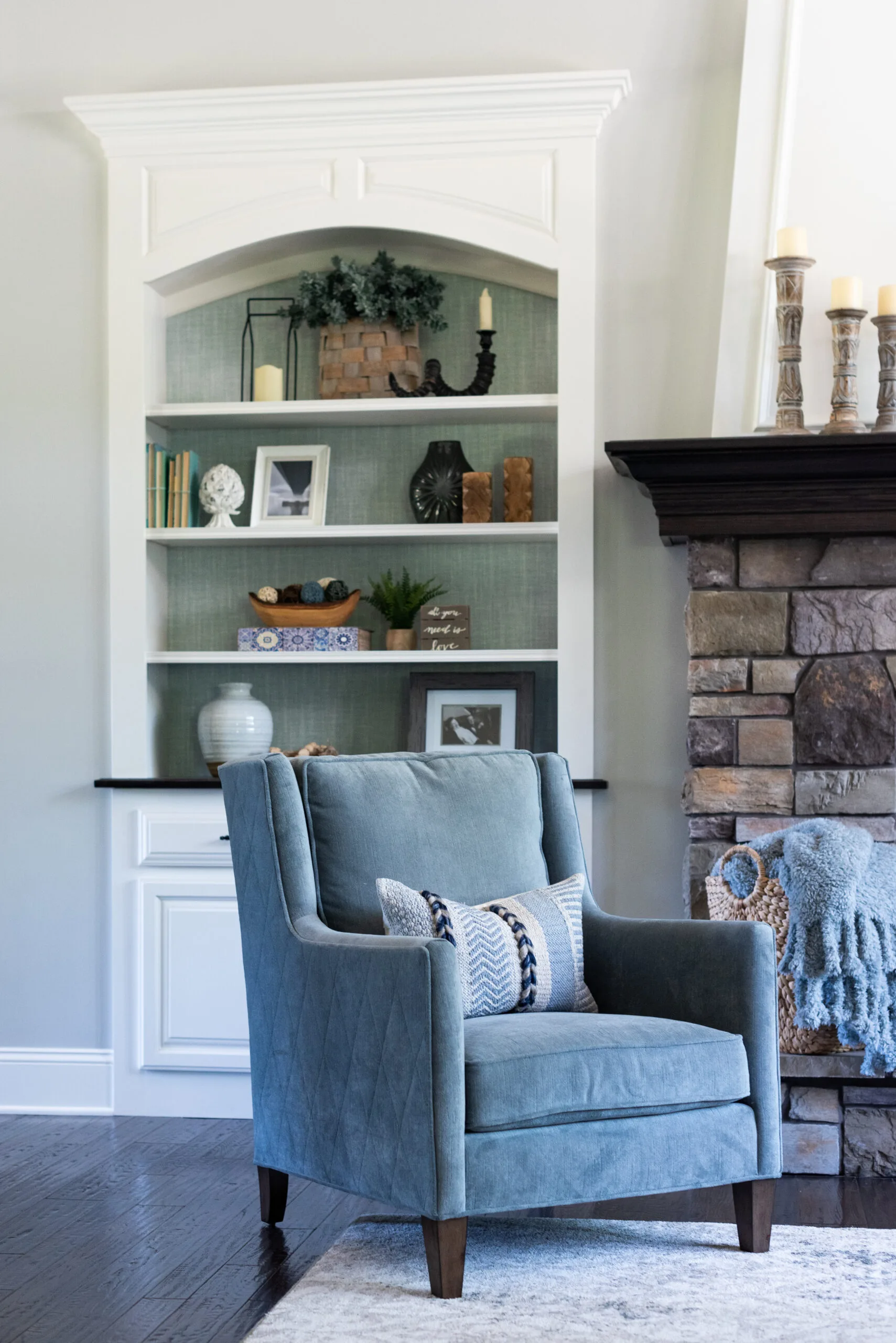 Living room view of white built-ins with turquoise wallpaper behind and a blue accent chair sitting in front