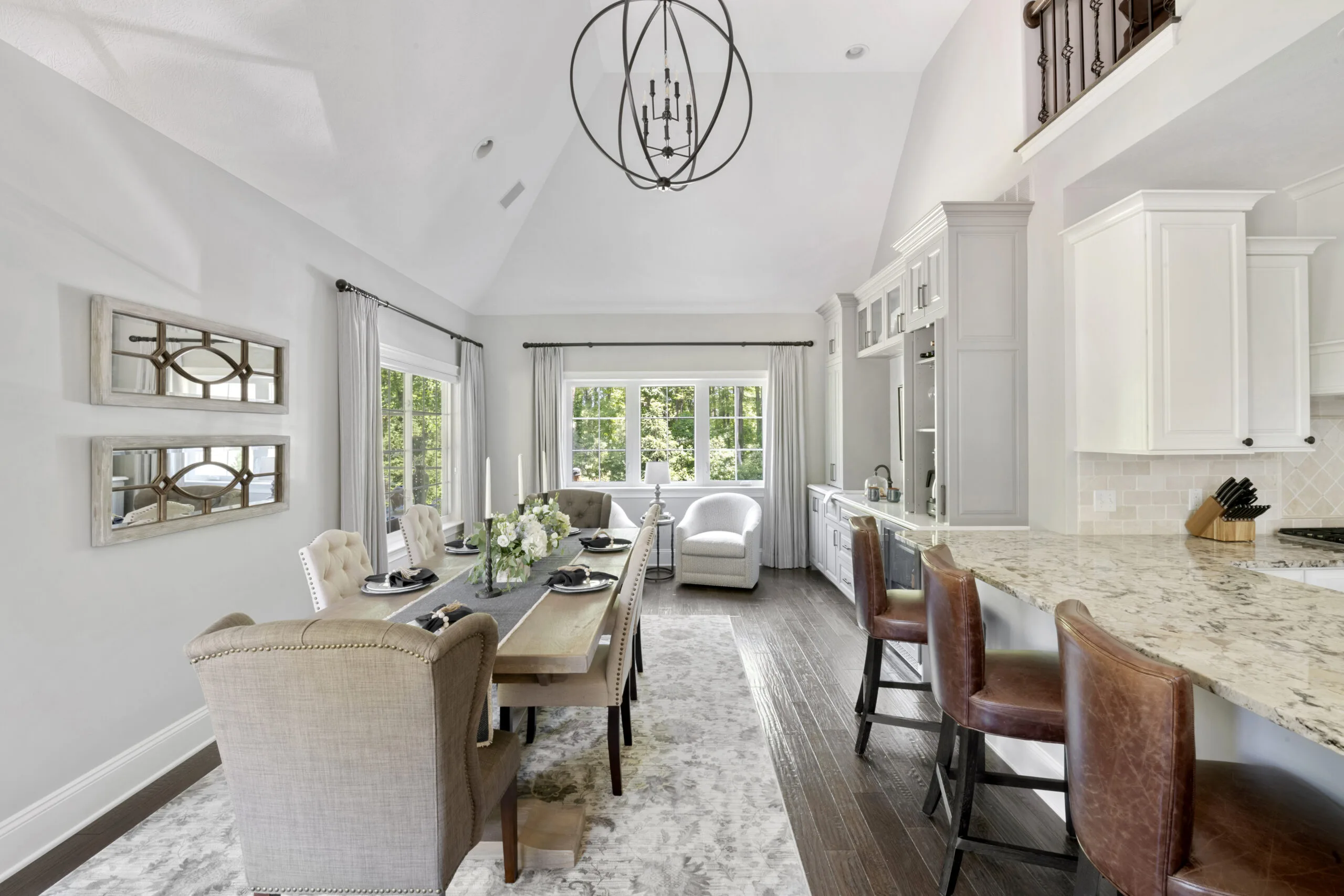 Dining room with a light wood table and gray accents to the left of a countertop with leather barstools