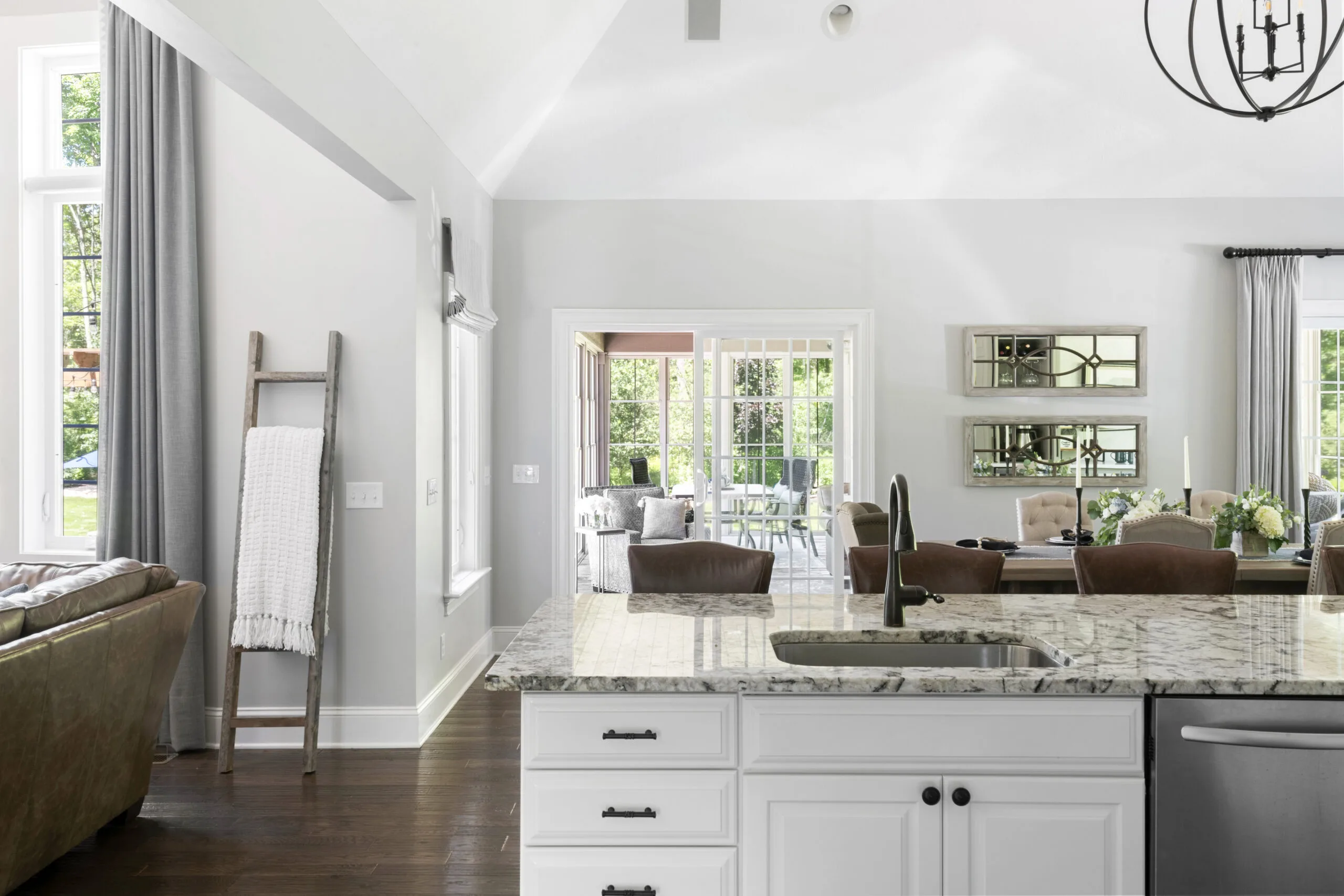 View from a kitchen sink into a dining room and sunroom with neutral color palettes