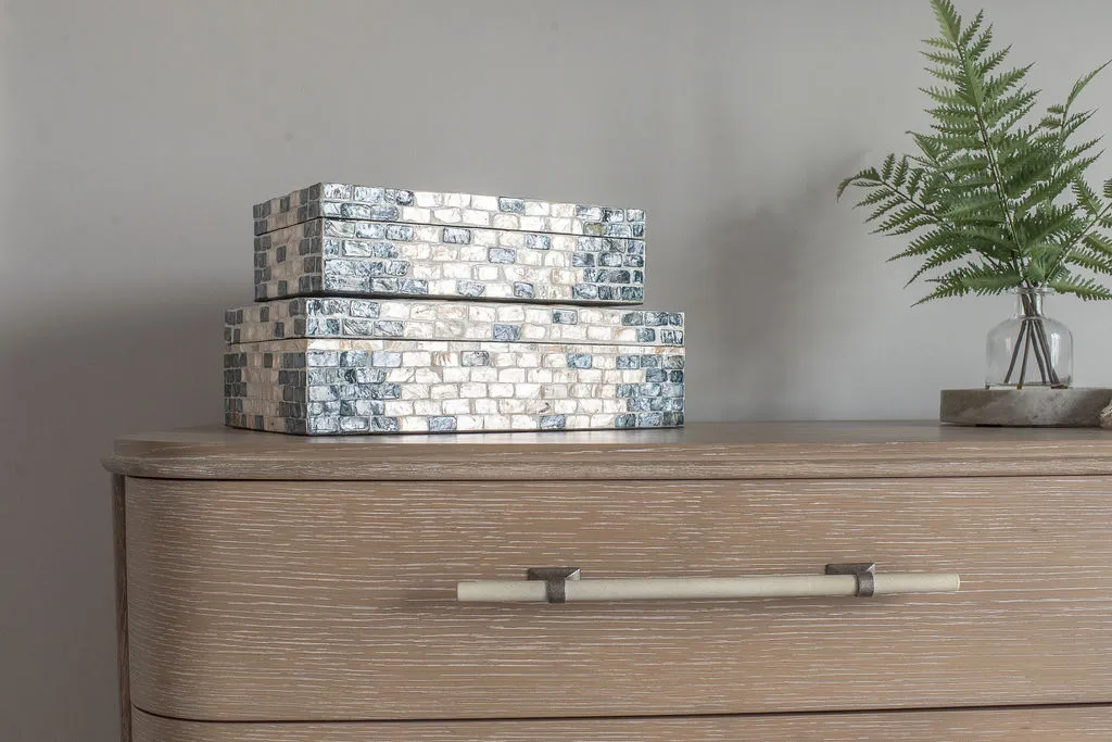 Close up image of a wooden dresser with blue and white boxes stacked on top and greenery to the right