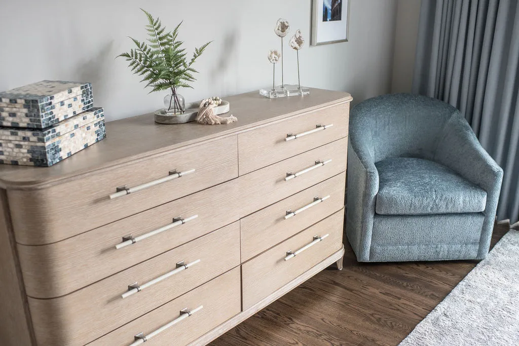 Light wood bedroom dresser with accessories on top and an aqua blue lounge chair resting beside in a corner