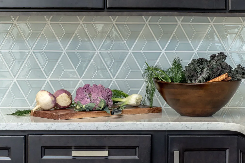Closeup of vegetables sitting on a wooden platter and in a bowl with a light blue geometric backsplash behind