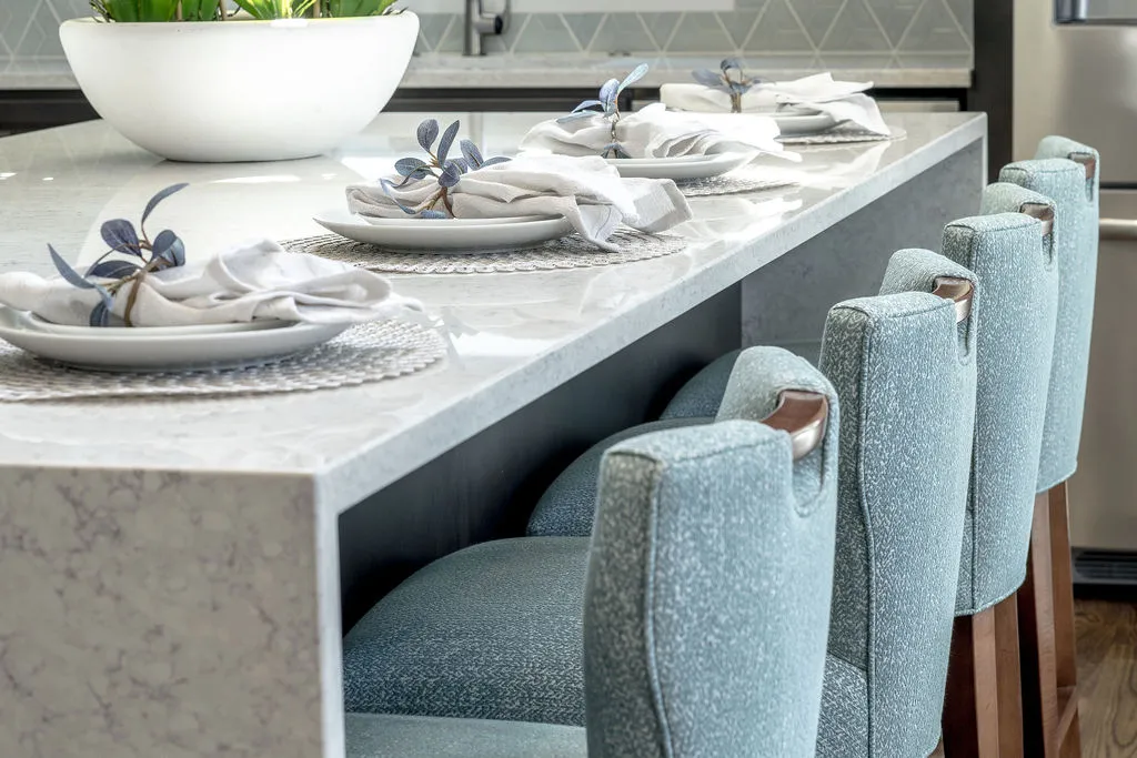 Island with waterfall countertops and aqua blue upholstered counter stools tucked beneath
