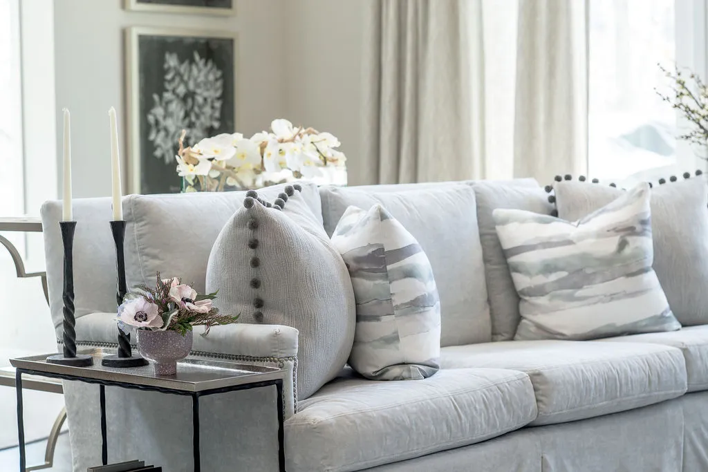 Light, neutral colored sofa with throw pillows and a wood/metal side table with accessories to the left