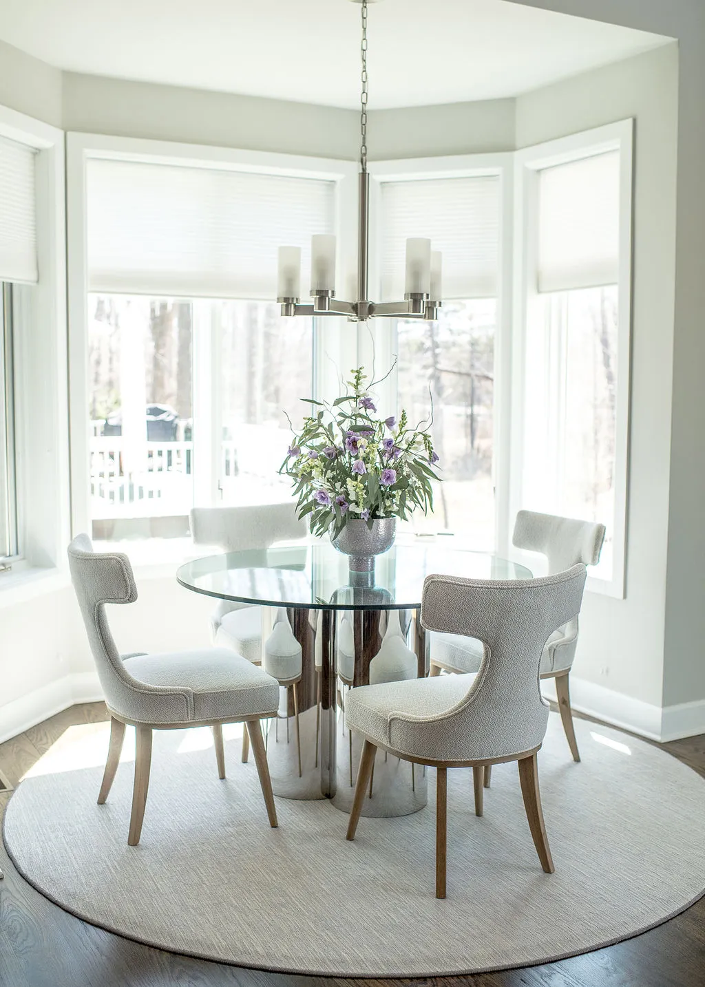Neutral colored dining nook with a round glass table and 4 neutral dining chairs on top a round rug