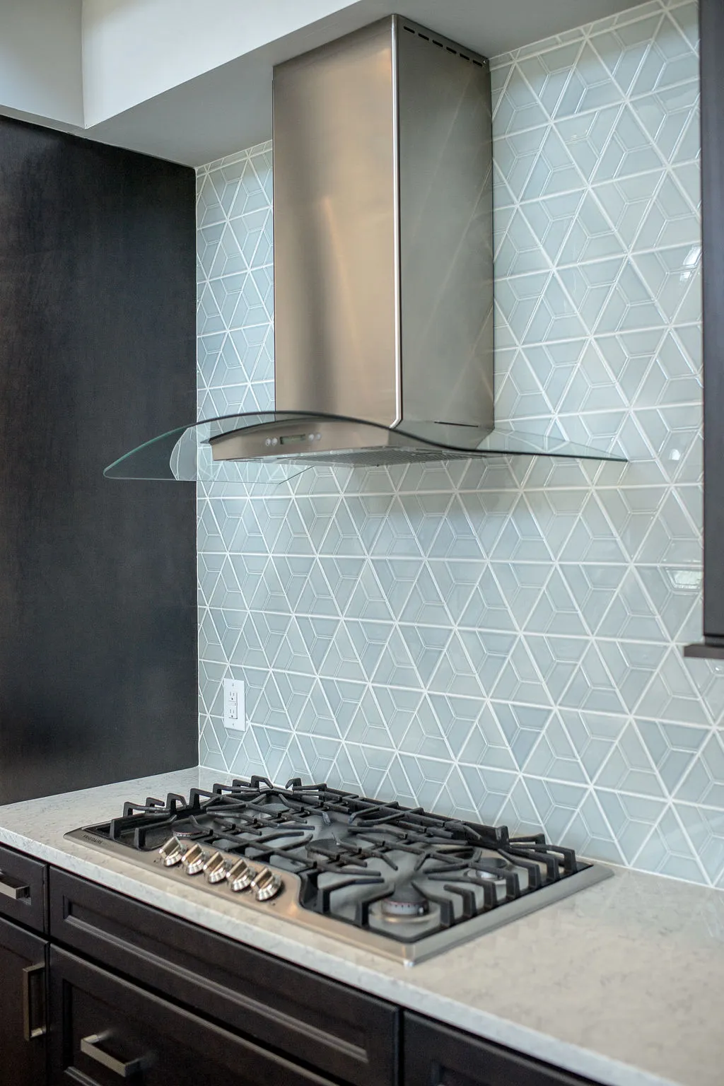 Gas stovetop with a metal and glass hood and a light blue, geometric backsplash