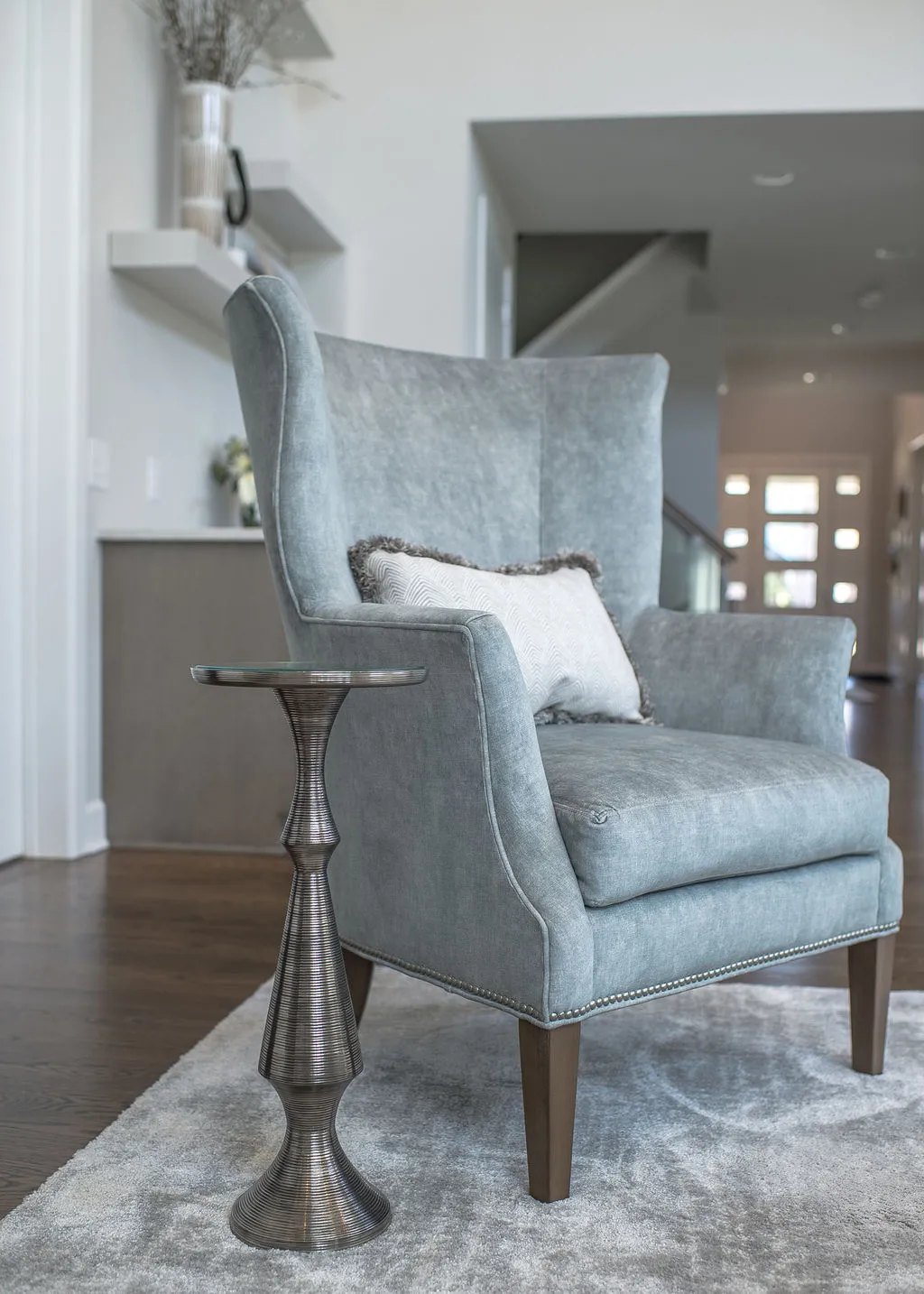 Close up image of a light blue, upholstered wing back chair with a silver side table sitting on top of a gray rug
