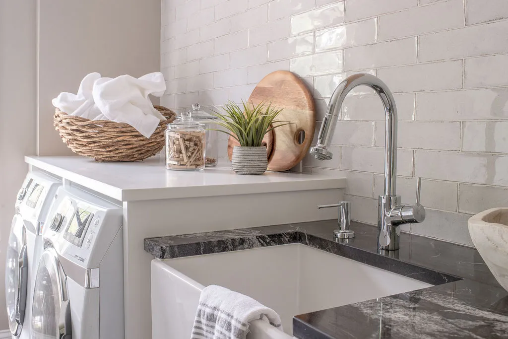 Close up image of farmhouse sink with a chrome faucet beside a washer and dryer