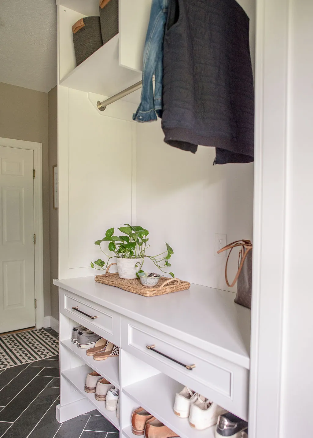White mudroom bench in a laundry room with coat, shoe, and basket storage