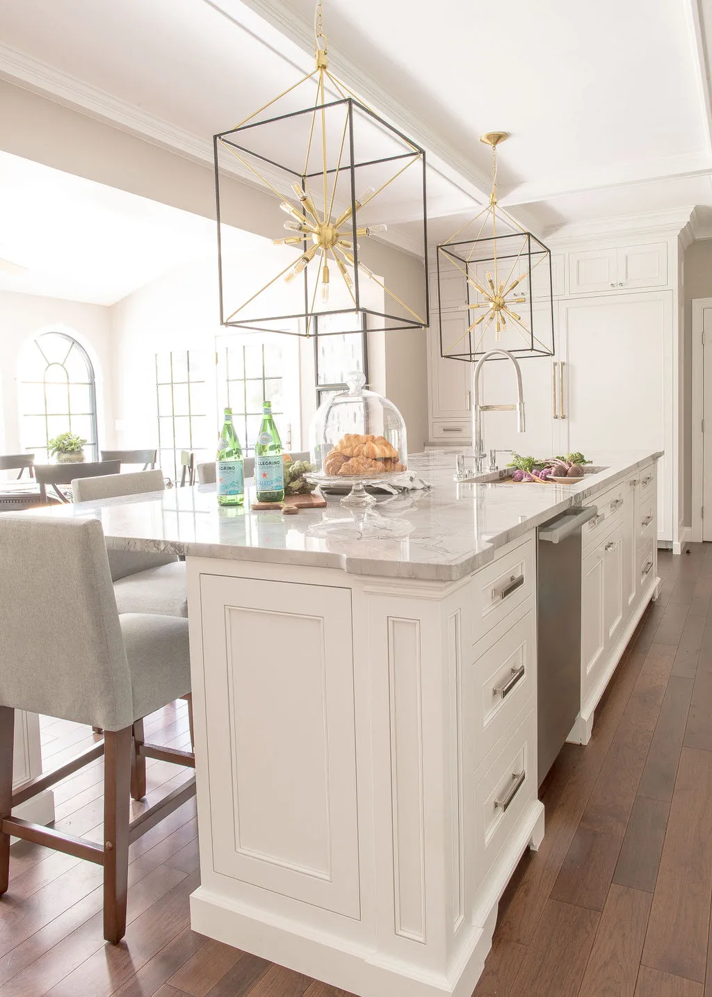 Large kitchen island with white cabinetry, silver hardware, and gray upholstered barstools tucked underneath