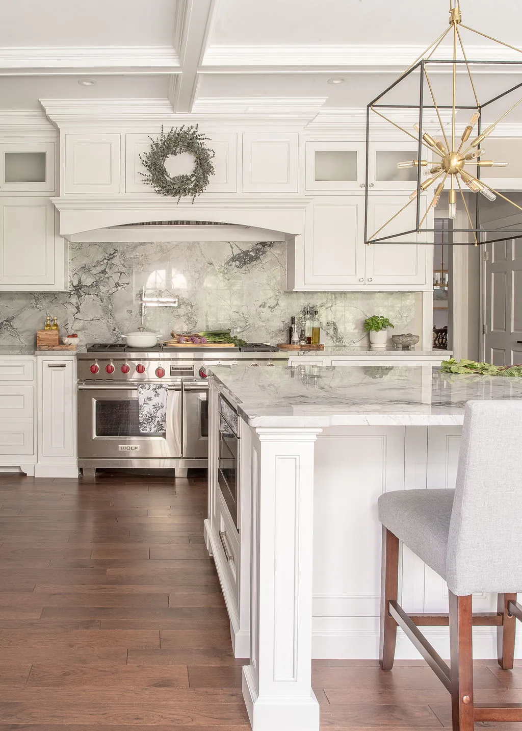 Large kitchen island with light gray barstools and a range and hood in the background