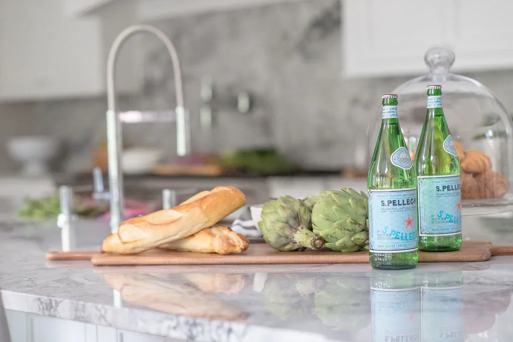 Bread board on a large kitchen island with a faucet and range in the background