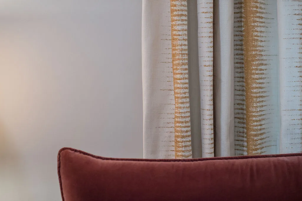 Close up image of a red, velvet headboard with yellow and white drapery behind
