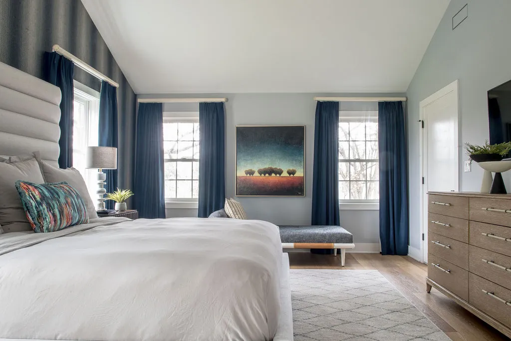 Guest bedroom with dark blue drapery and wallpaper, and light wood tones