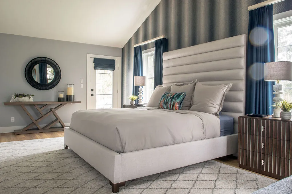 Bedroom with dark blue wallpaper and drapery, an upholstered white bed, and a console table with a round mirror above