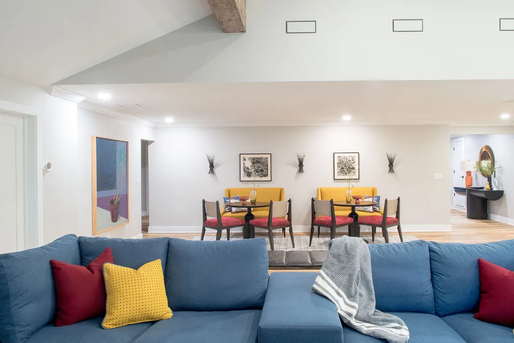 Living room with a blue sofa and red/yellow pillows, with a seating area in the background
