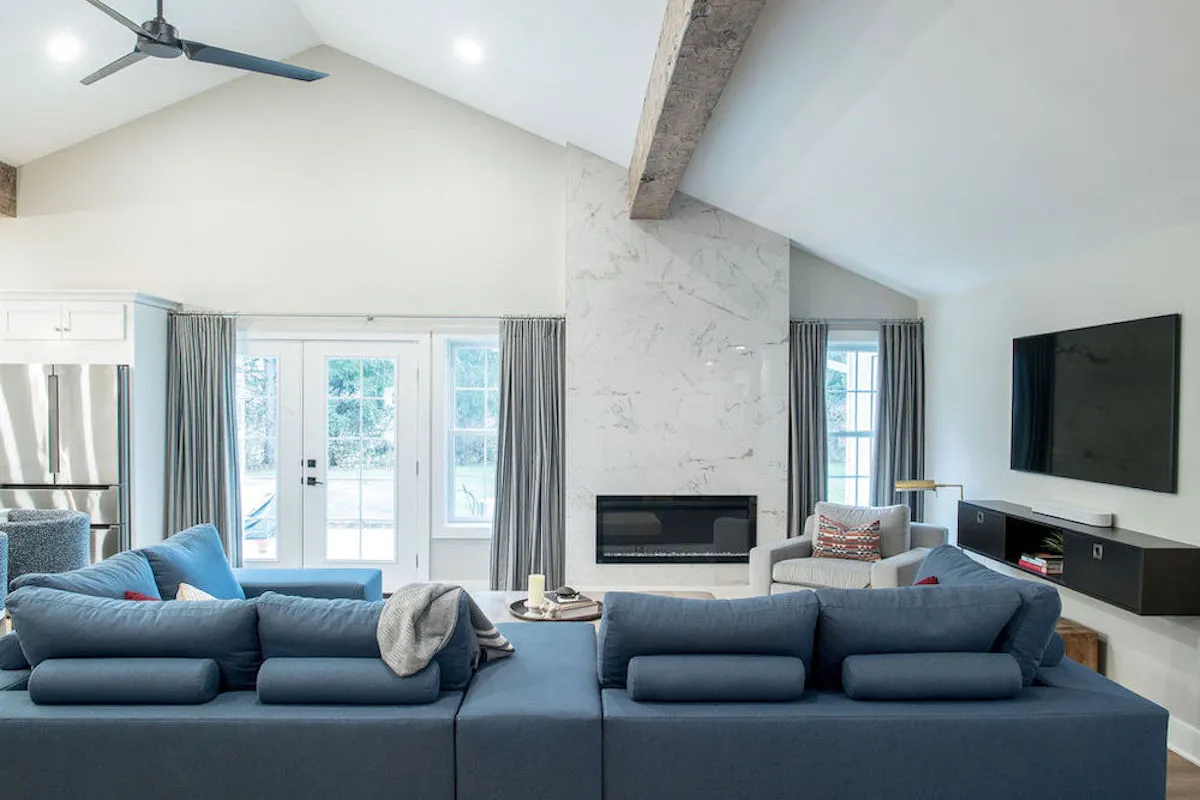 Living room with a blue sofa in front of a white stone fireplace and light blue drapery panels