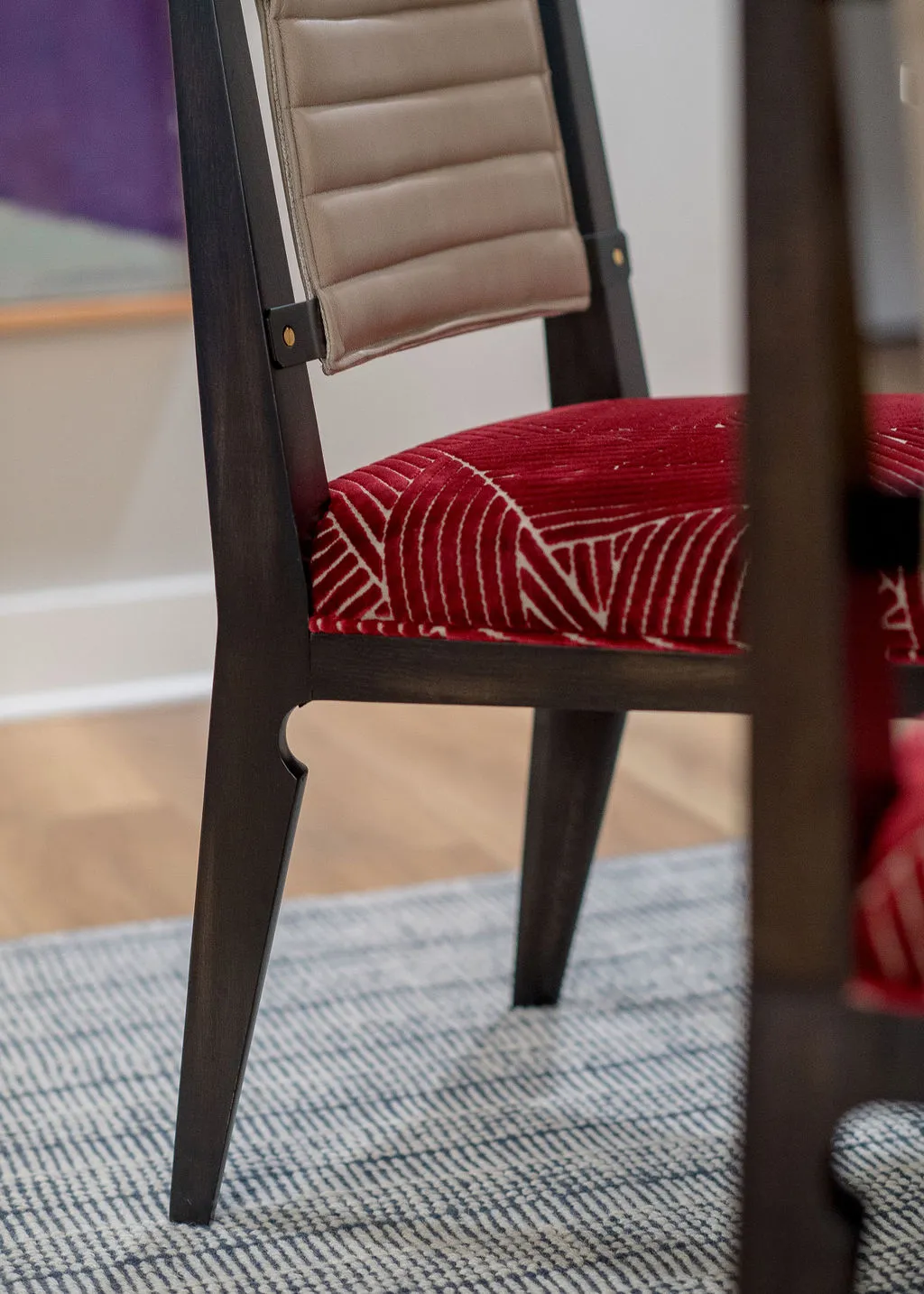 Close up image of a dining chair with a patterned red seat, leather back, and wood frame