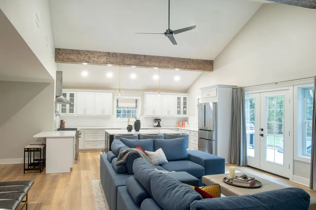 Overview of a neutral kitchen with a wooden beam and a living room with a blue sofa and light coffee table