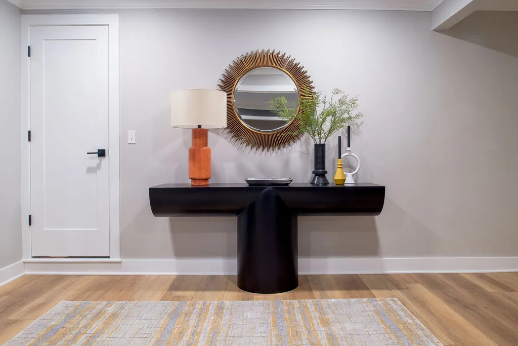 Long black table in a foyer with a round mirror above and vases with greenery sitting on top