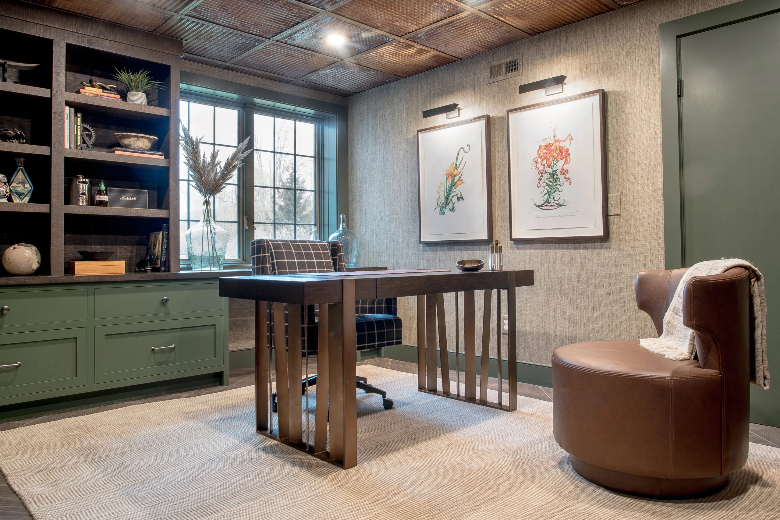 Overview of an office with a wooden desk, desk chair and lounge chair, built-in cabinetry, window, and artwork