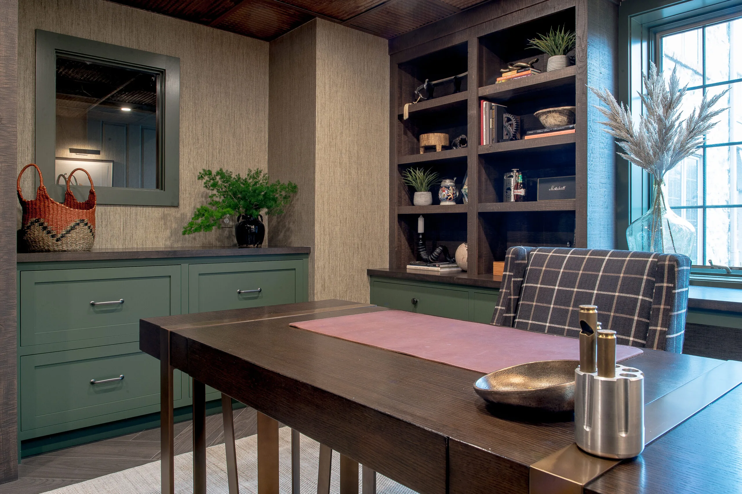 Close up image of a wooden desk with green cabinet drawers and stained open shelving in the background