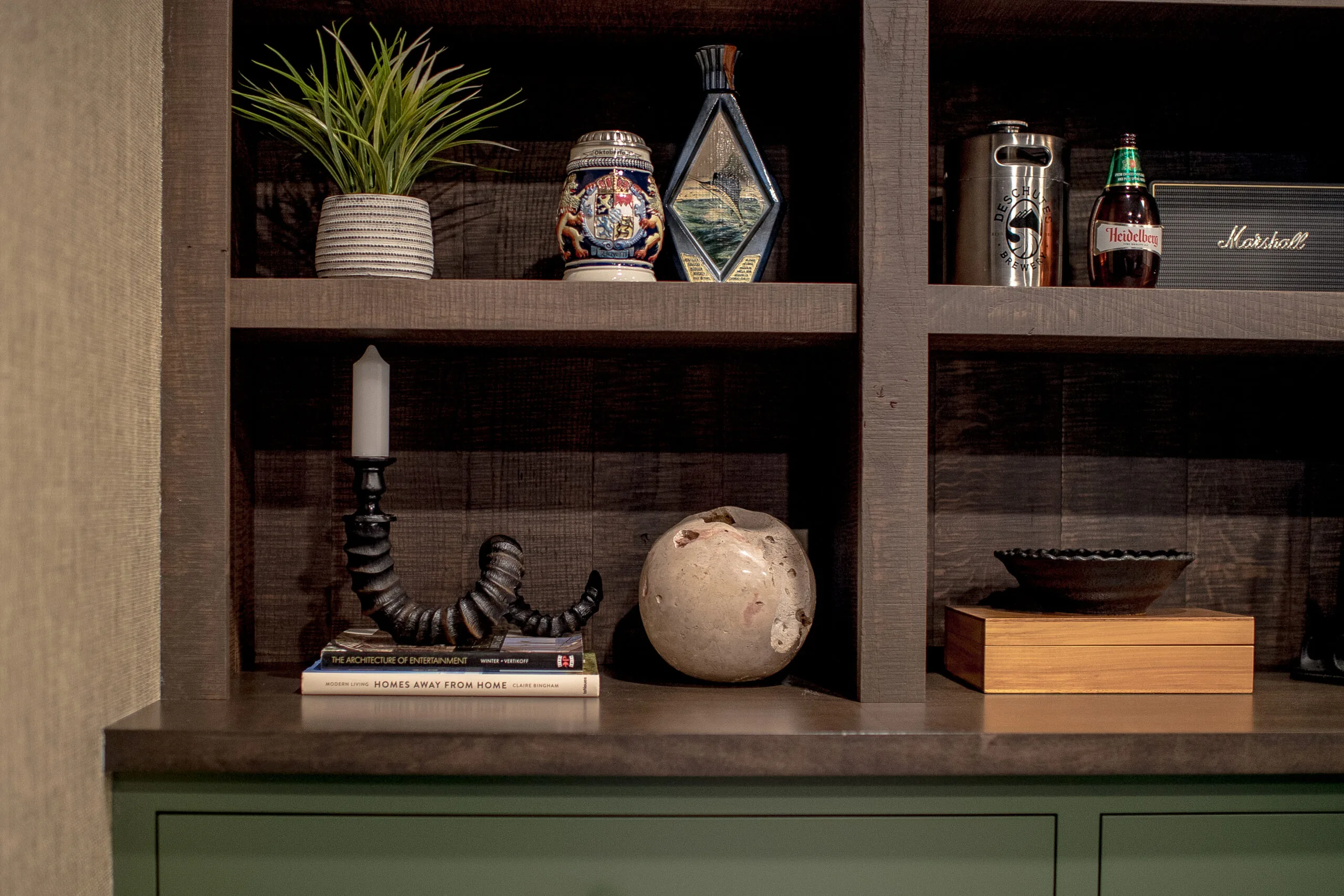 Close up image of dark, stained open shelving with a variety of accessories on each shelf and green cabinetry underneath
