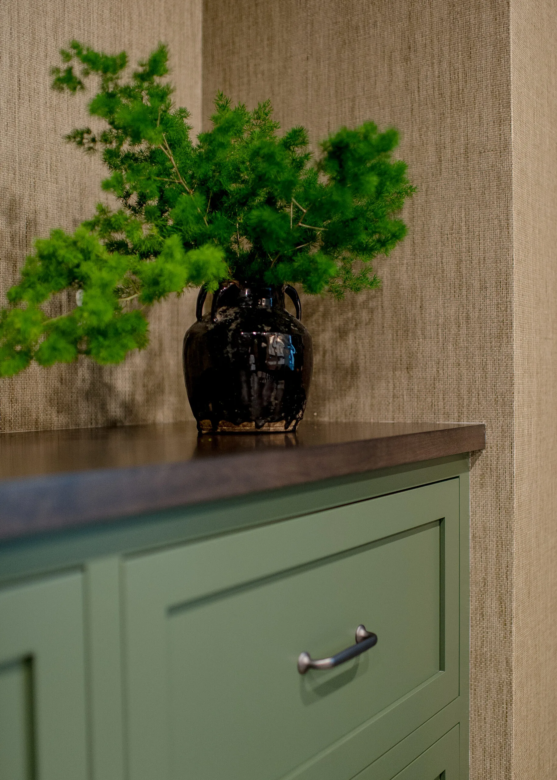 Close up image of green base cabinets with a wood countertop and a vase with greenery sitting on top