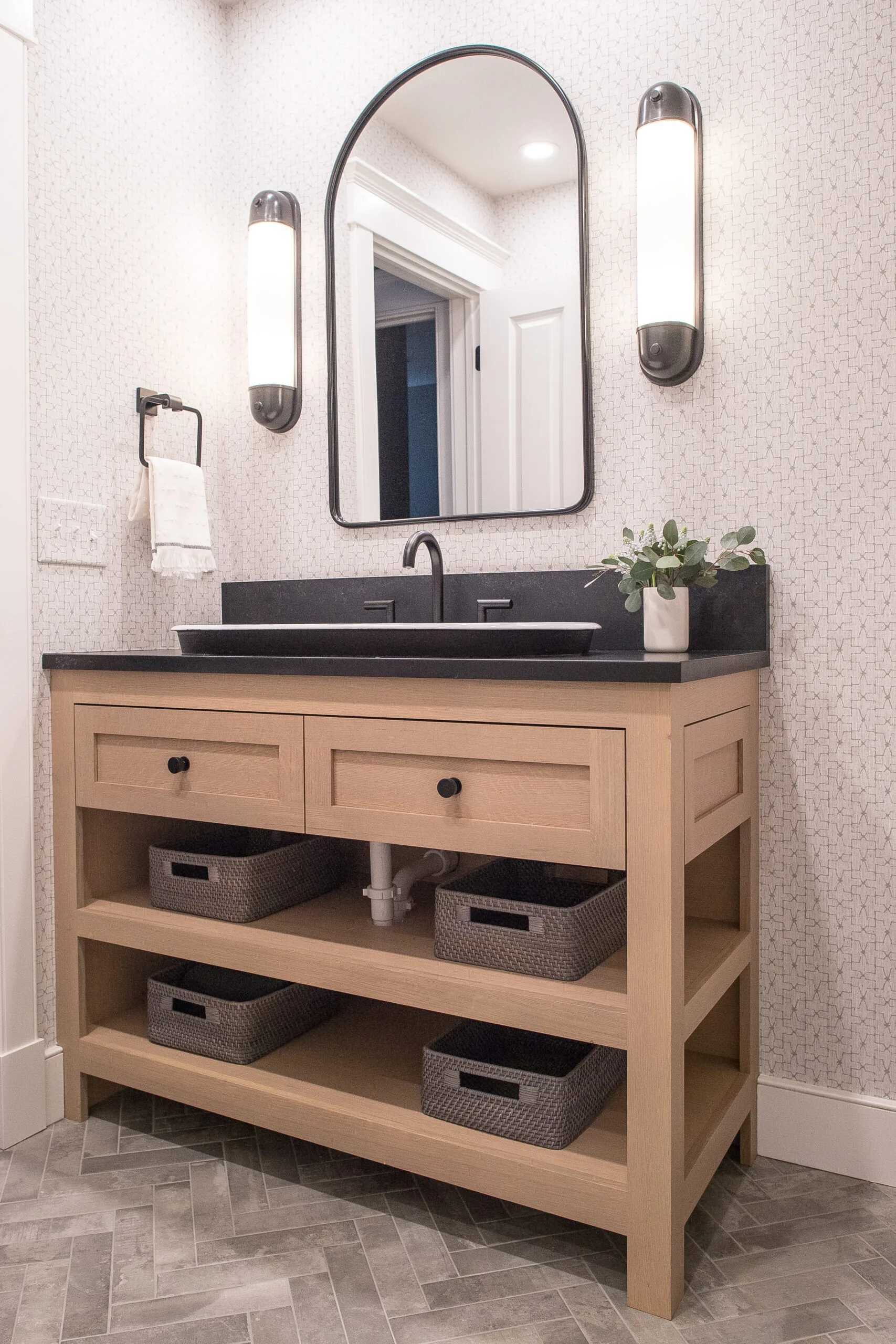 Bathroom vanity with a black countertop and light stained base. A mirror with two sconces above