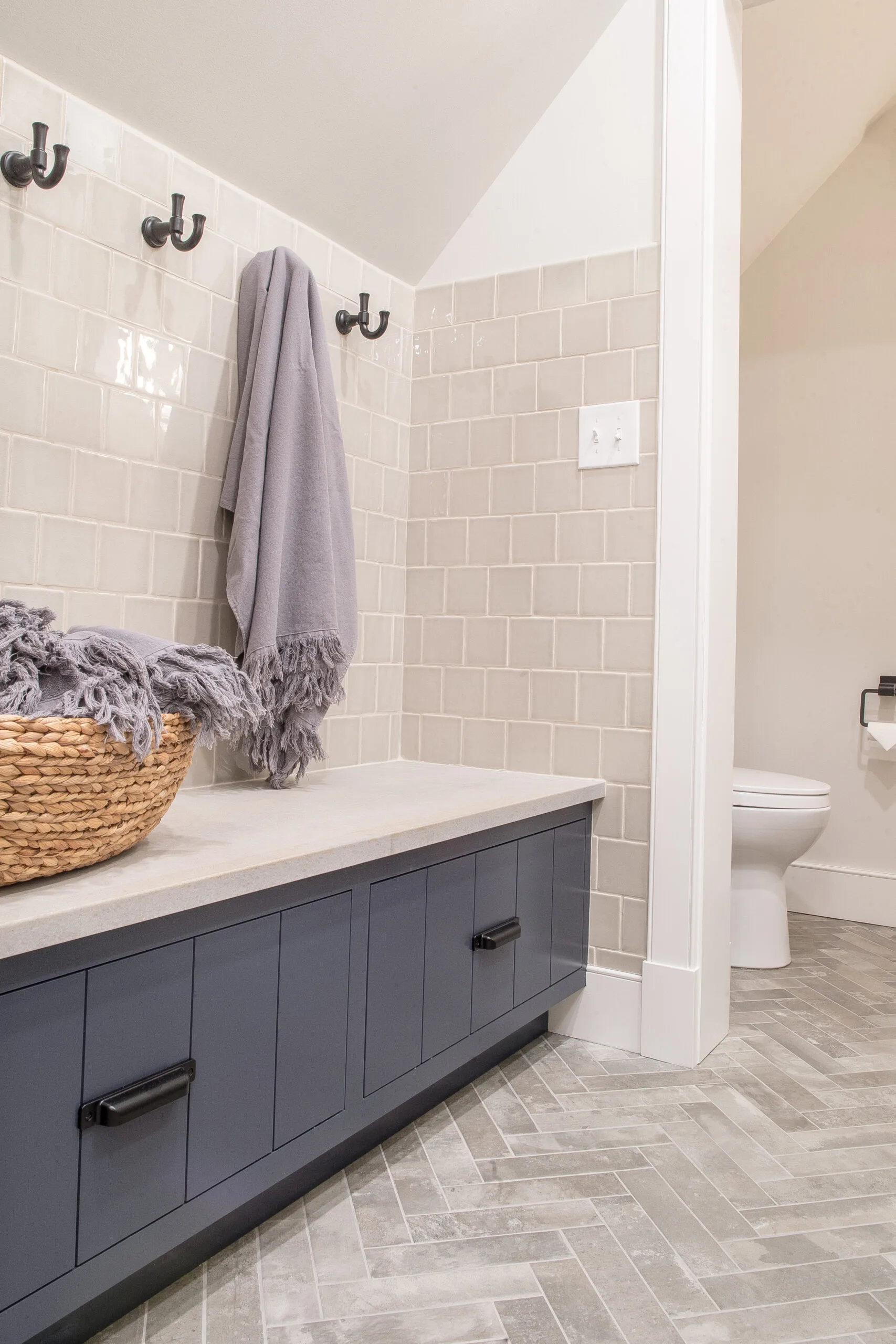 Blue storage bench in bathroom with a white top and hooks above. As basket sitting on top of the bench