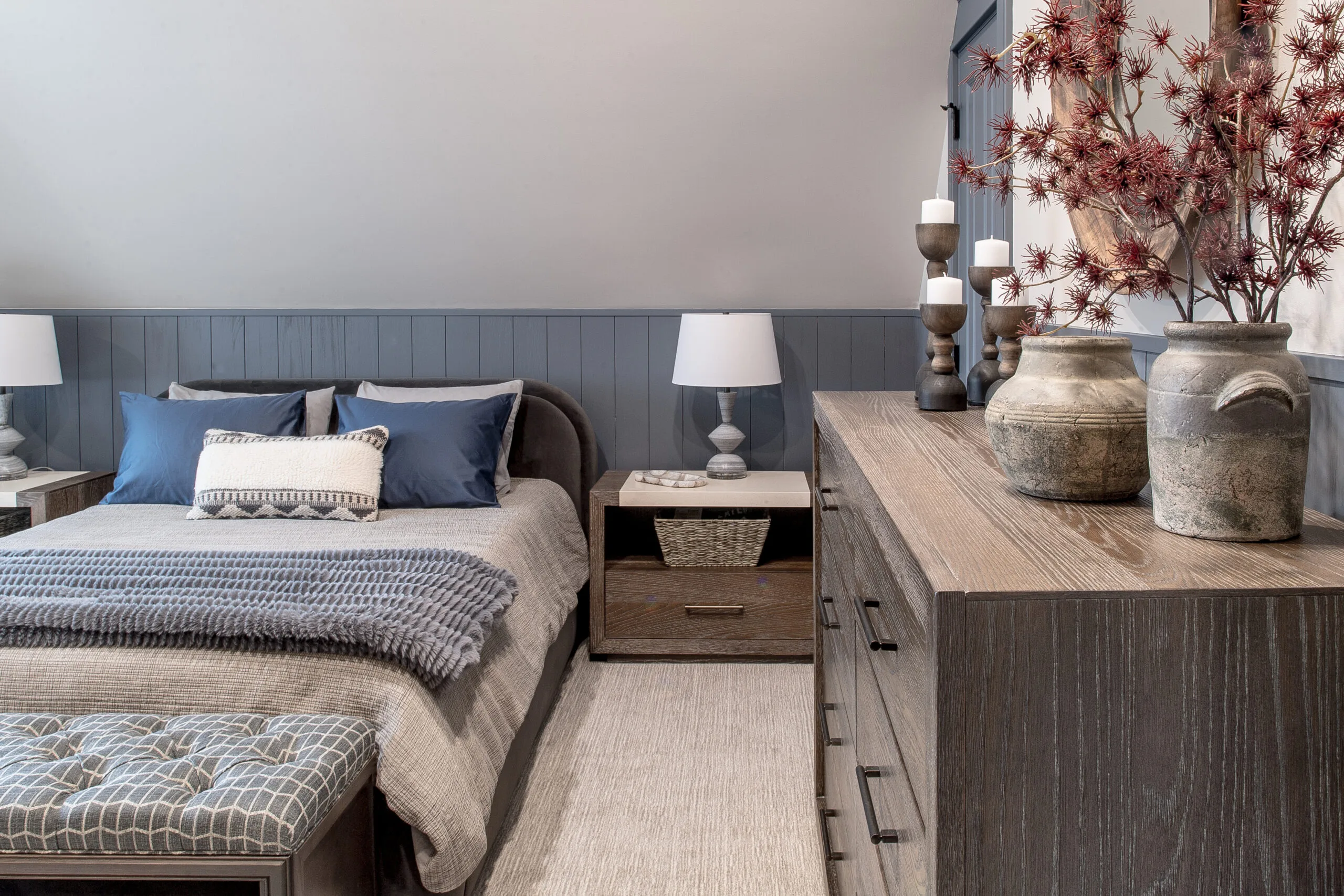 Image of a navy and neutral bedroom looking at a chest, a bed with wooden side tables, and lamps on top