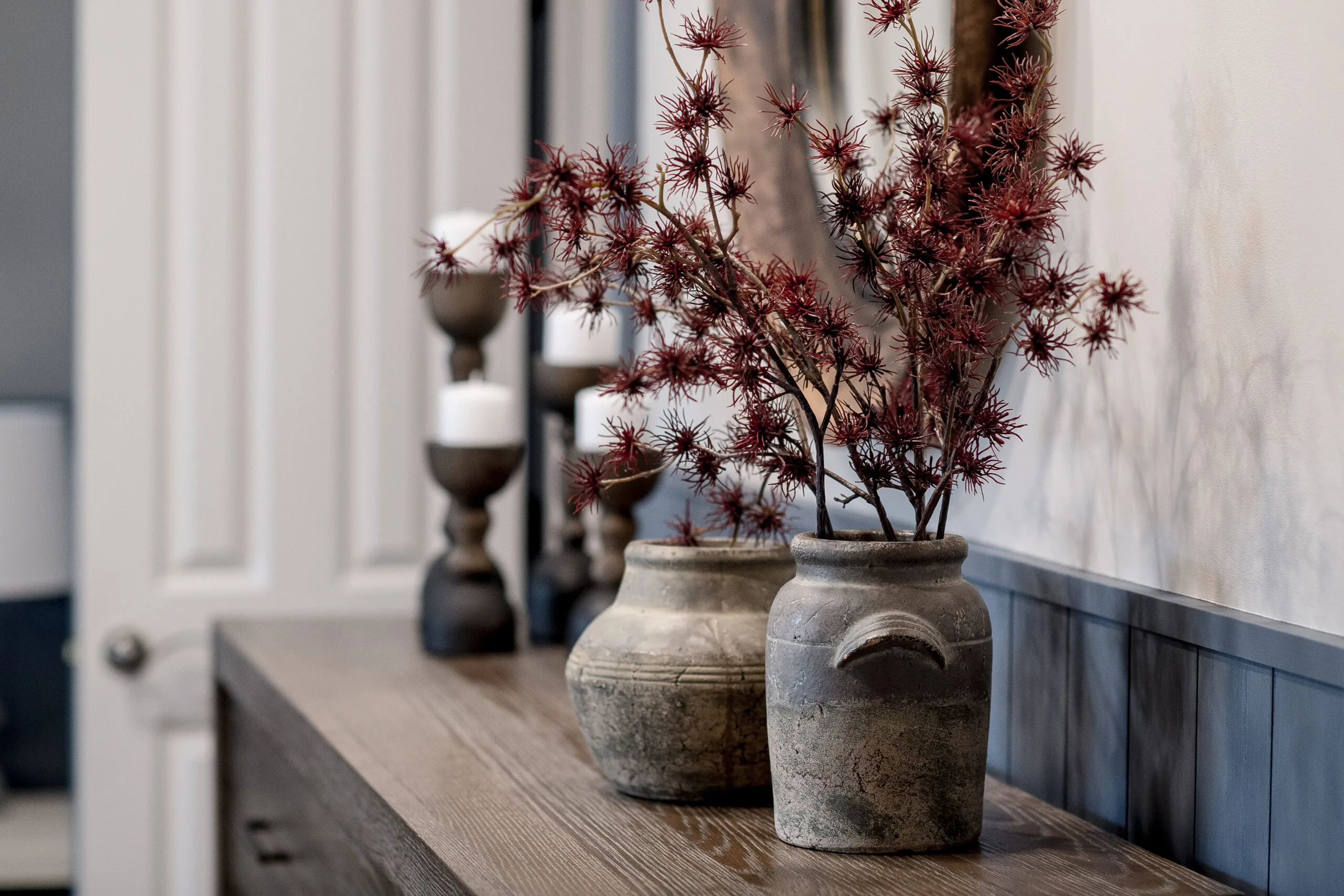 Close up photo of the top of a bedroom dresser with black candle sticks, vases, and red florals