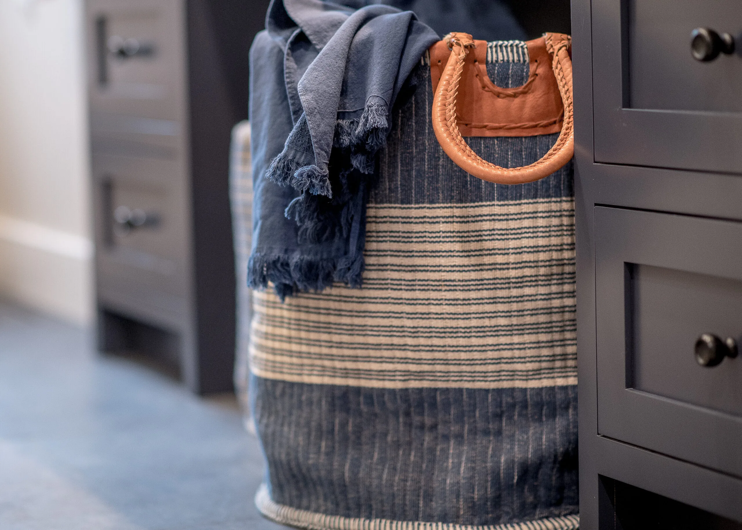 Image focusing on a navy and tan striped laundry basket tucked underneath blue cabinetry