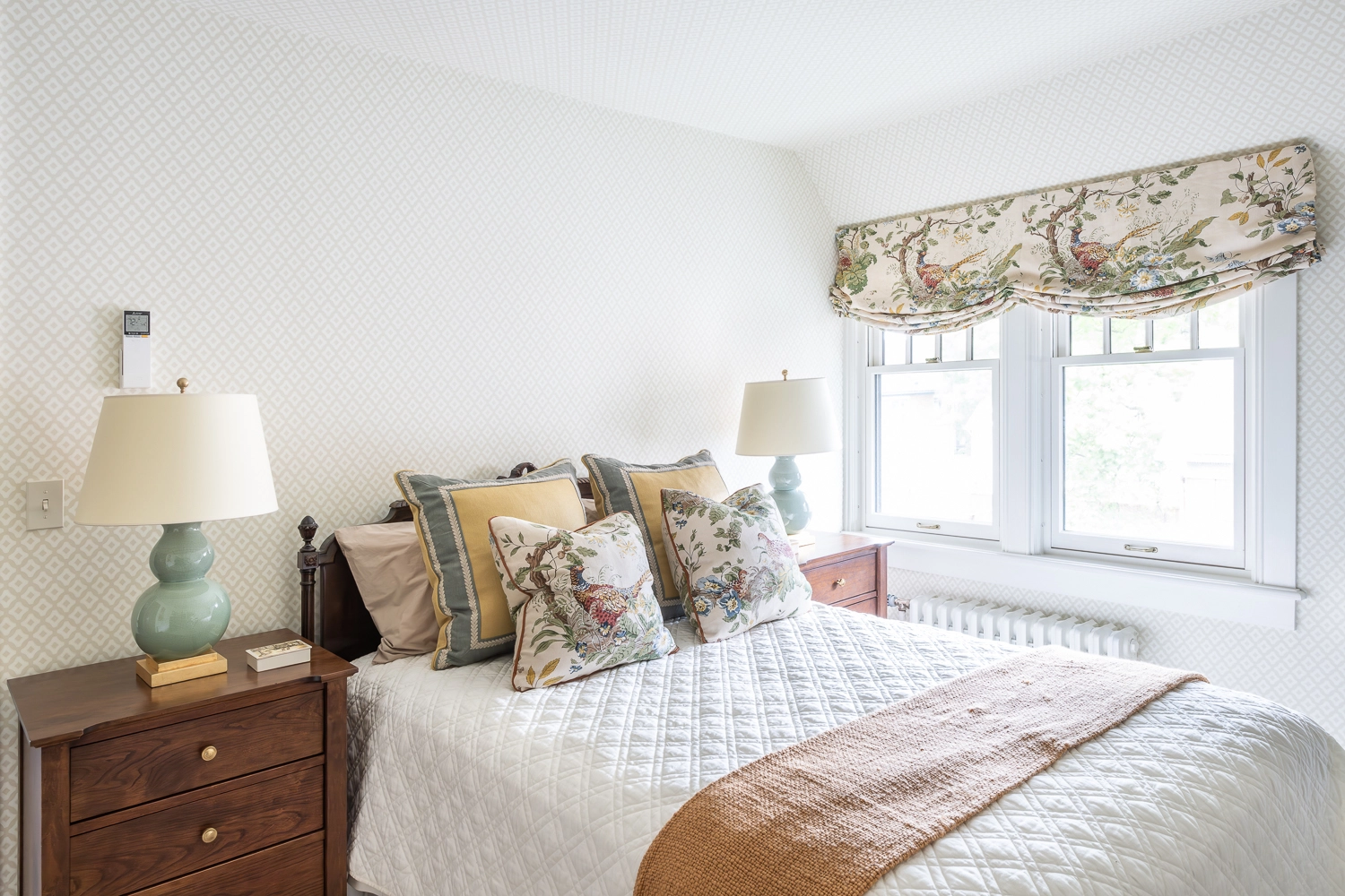Image of bed with white quilt, orange throw, and pillows