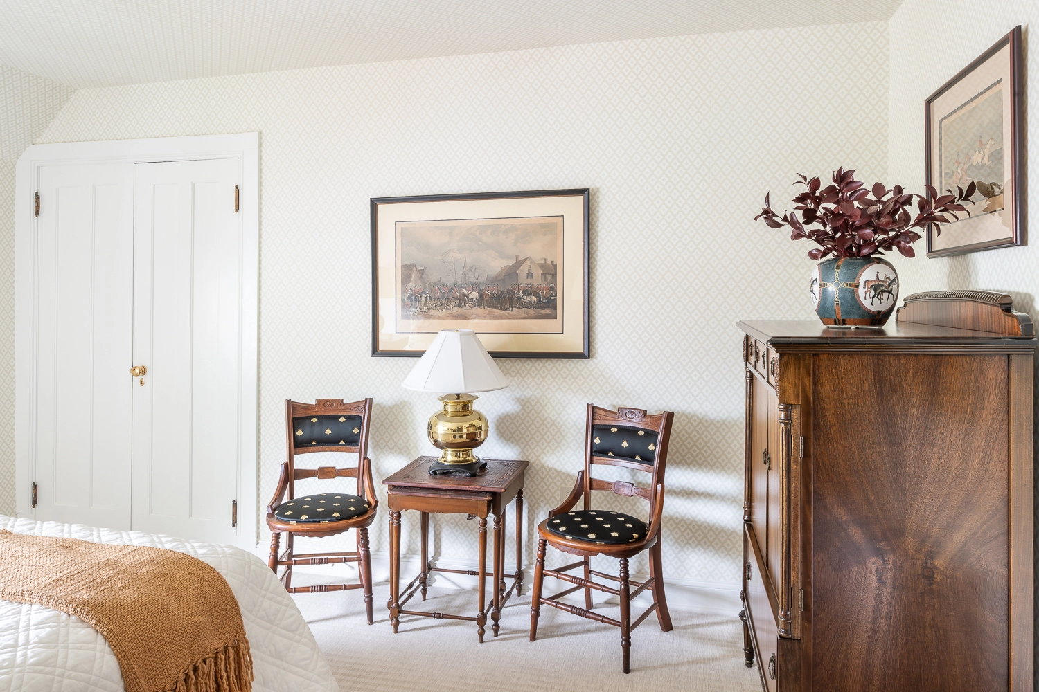 Image of two upholstered chairs aside a wooden with a lamp, artwork above