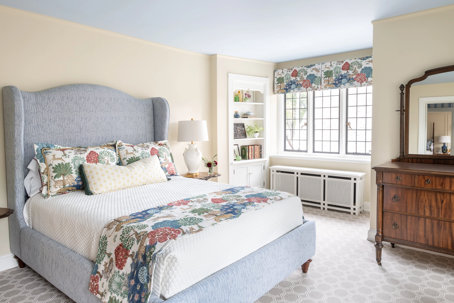 Upholstered blue bed with a pattern blanket, in front of windows