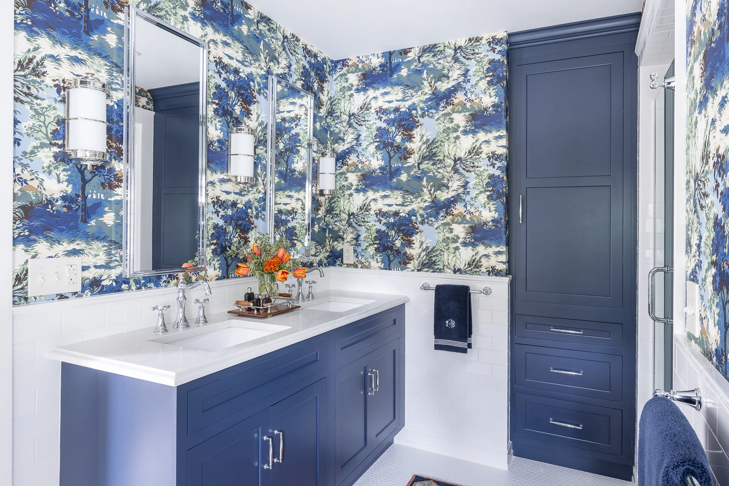 Bathroom with blue cabinetry, blue/white wallpaper, and a double sink