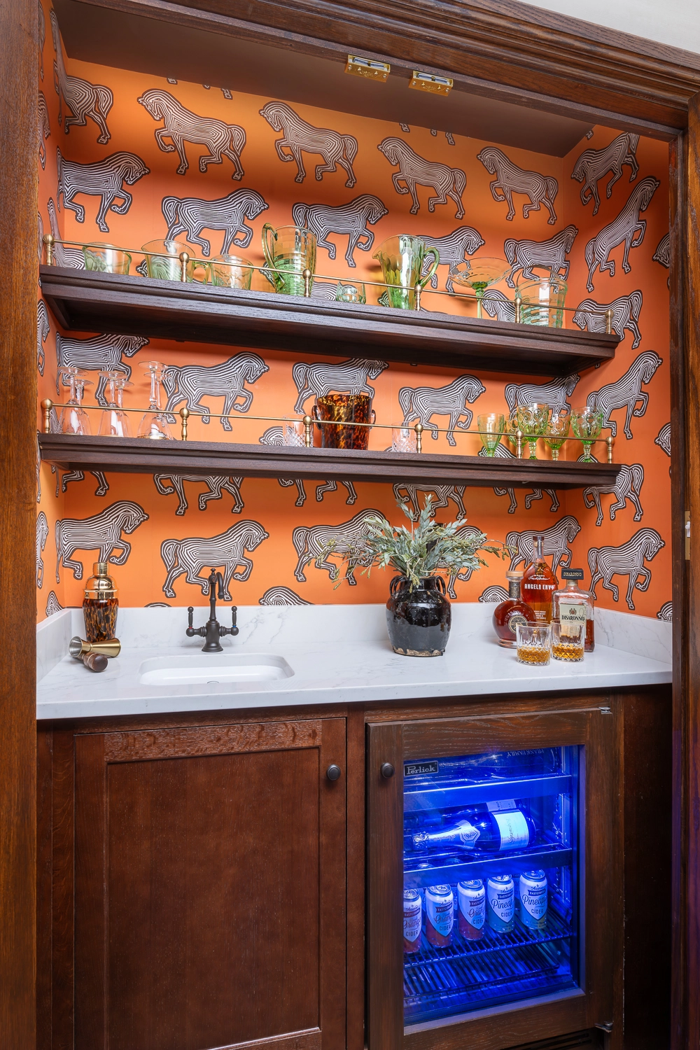 Bar built-in to a closet with orange tiger wallpaper, floating shelves, and barware
