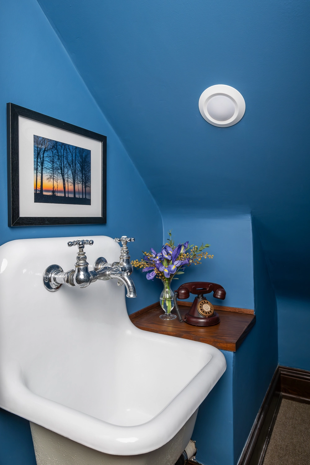 Blue storage closet with utility sink and rotary phone on ledge beside it