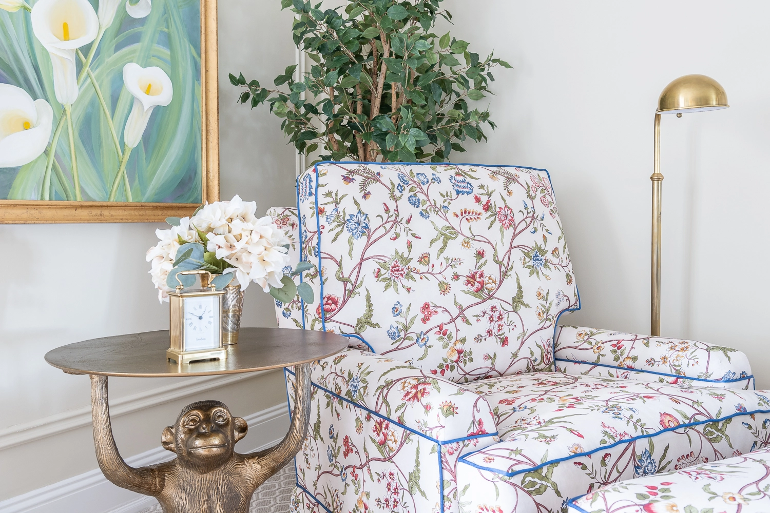 Upholstered chair next to a brass monkey side table with florals on top