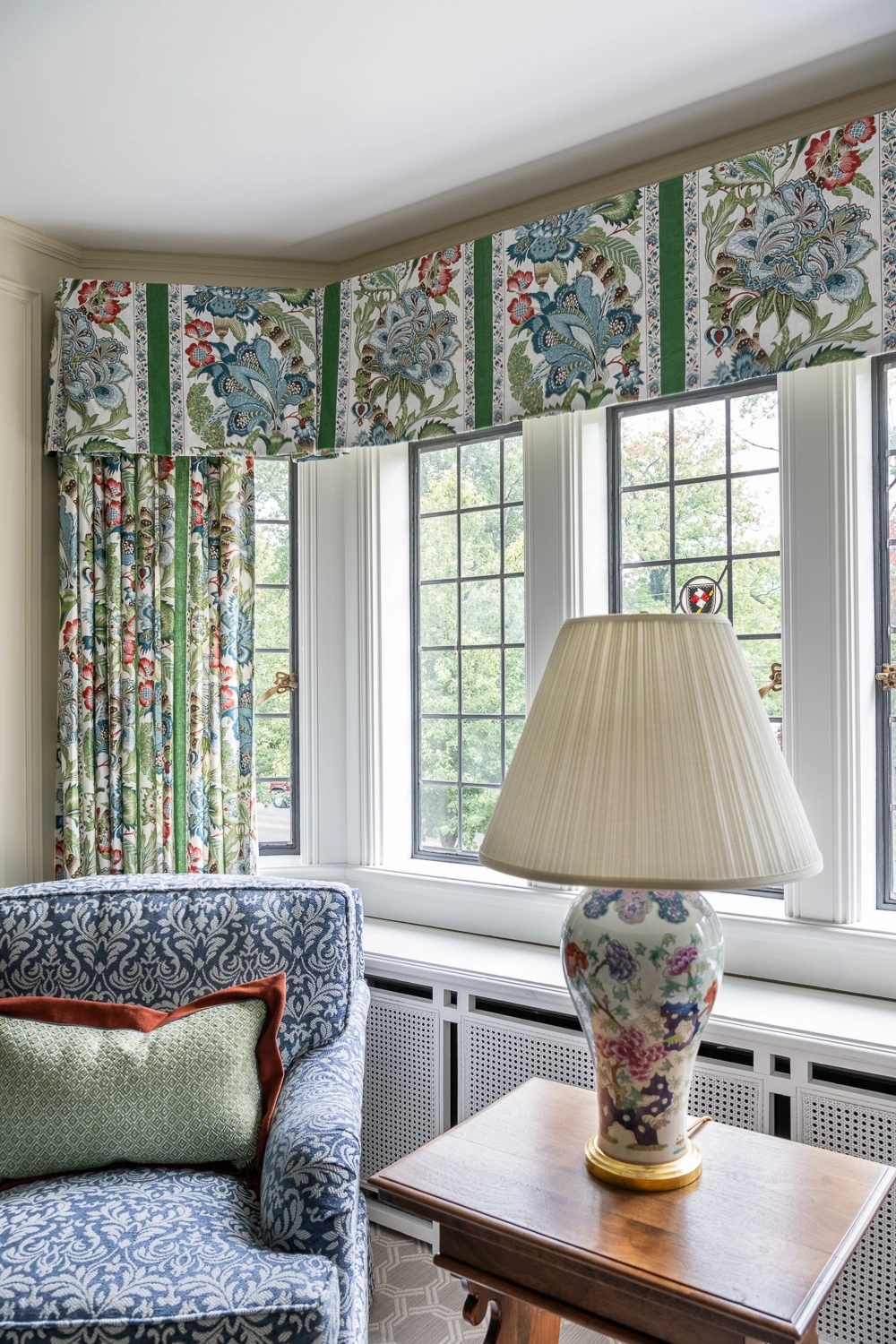Window with a green, patterned pleated valance behind a sofa table, lamp, and side chair