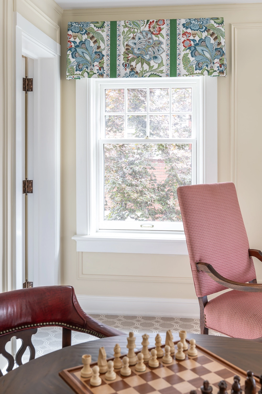 Window with a green patterned valance and red upholstered chair
