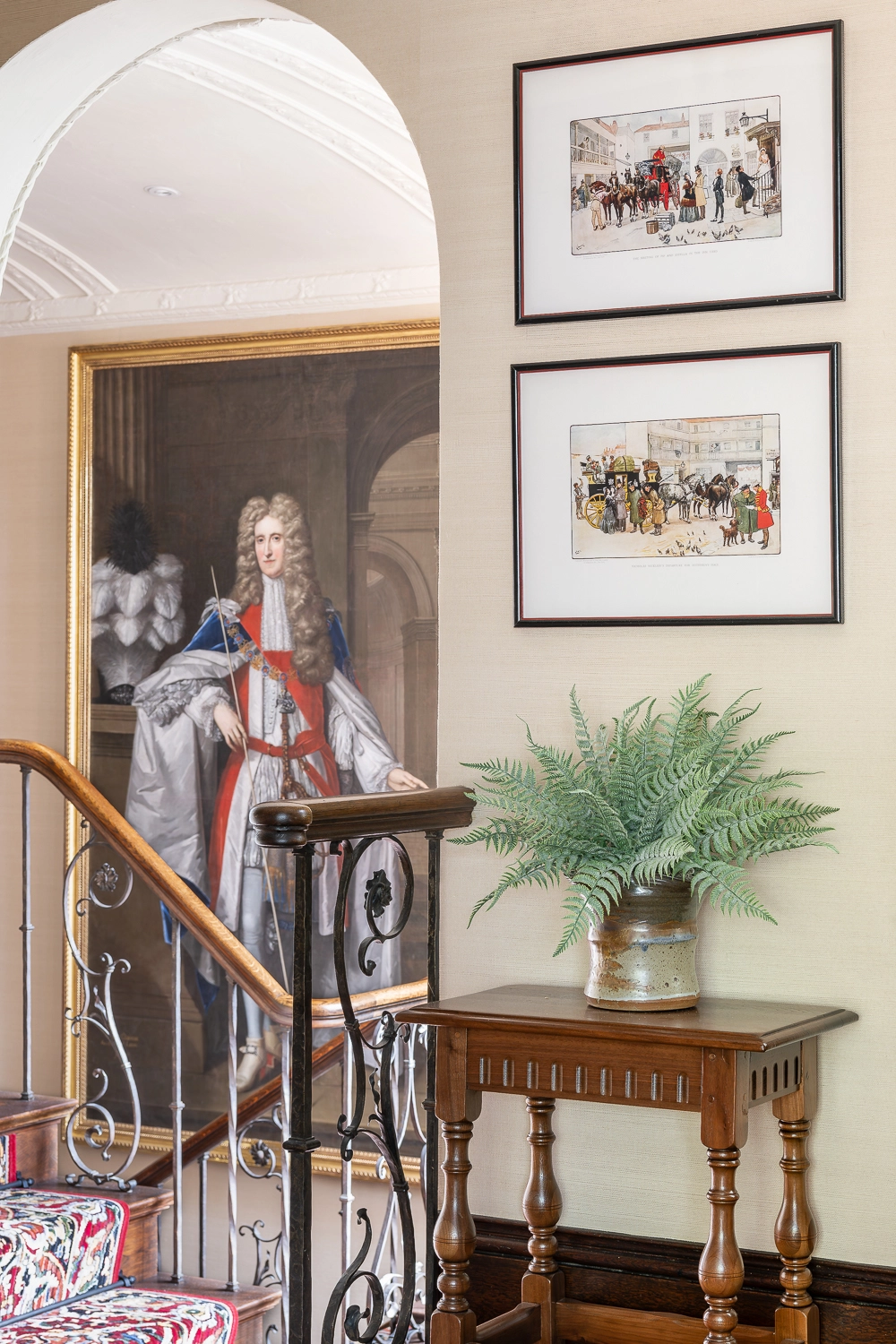 Small wooden table with greenery on top and artwork above, a large portrait behind in the adjacent room