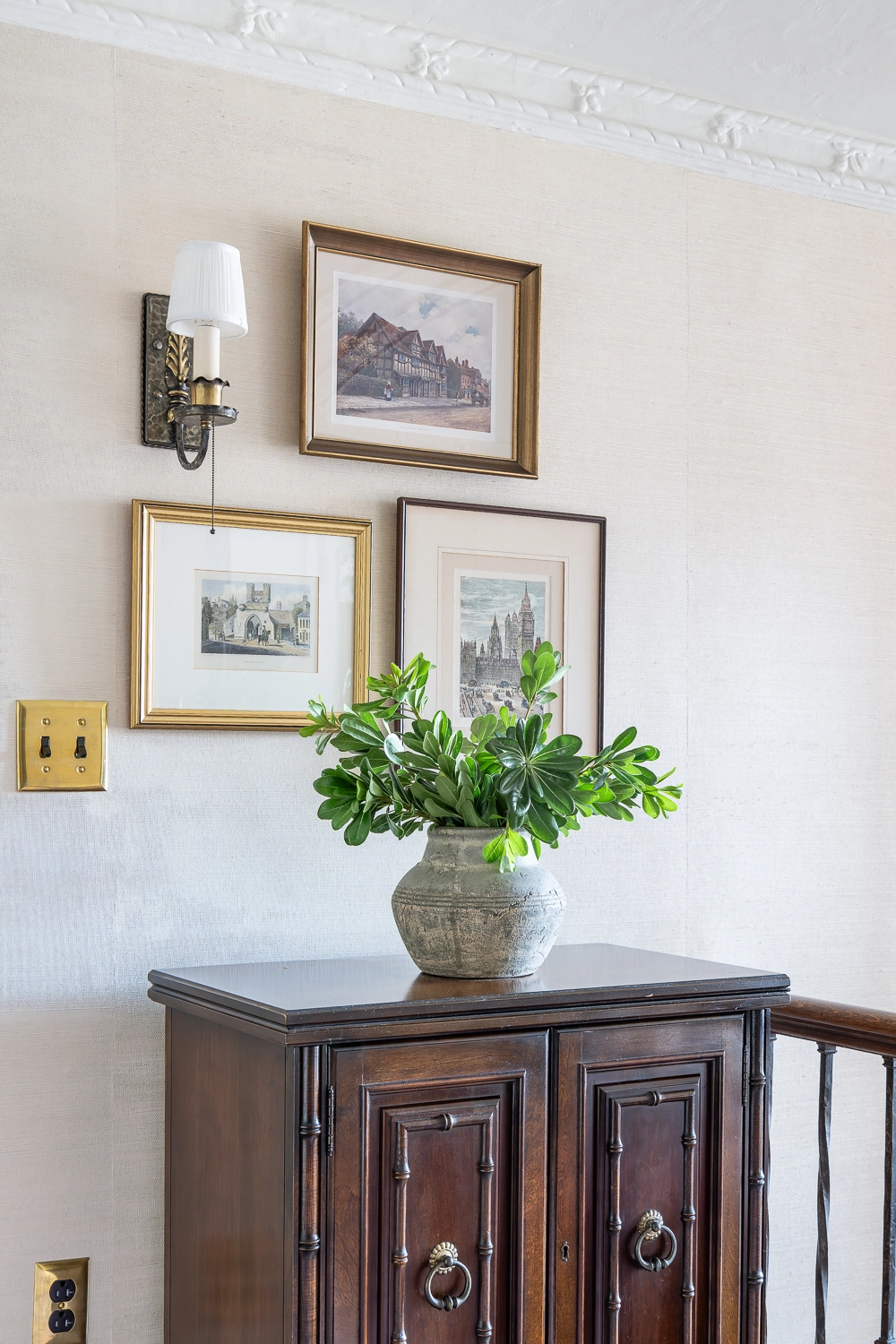 Wooden chest with greenery sitting on top and 3 small pieces of artwork above
