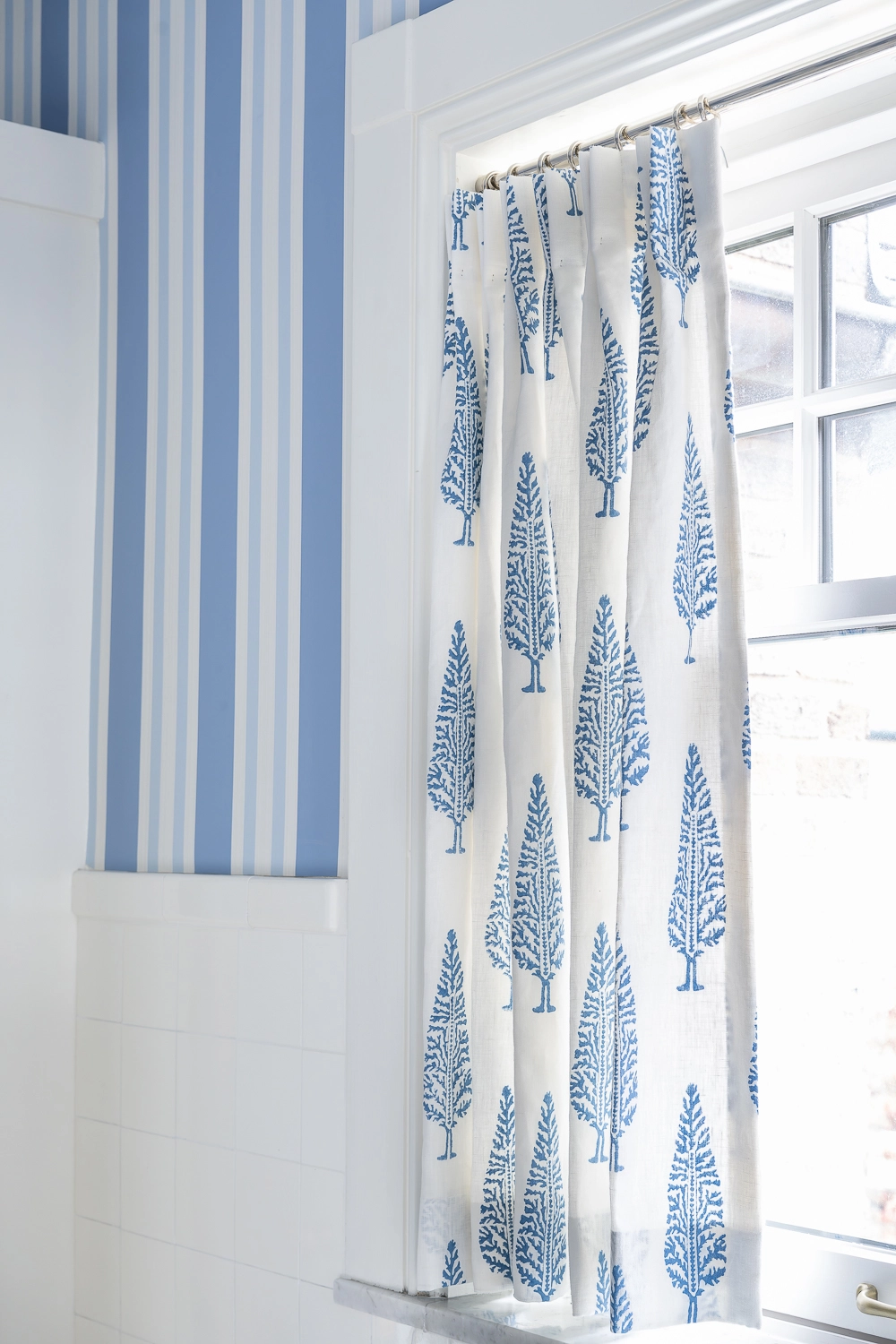 Blue and white striped bathroom focusing on a blue patterned drapery panel of a small window