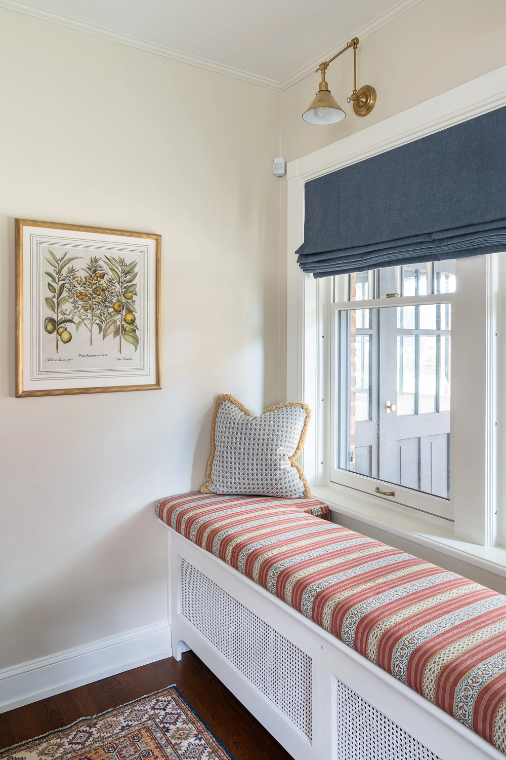 Image of a striped window seat with a pillowin front of a window with a blue valance