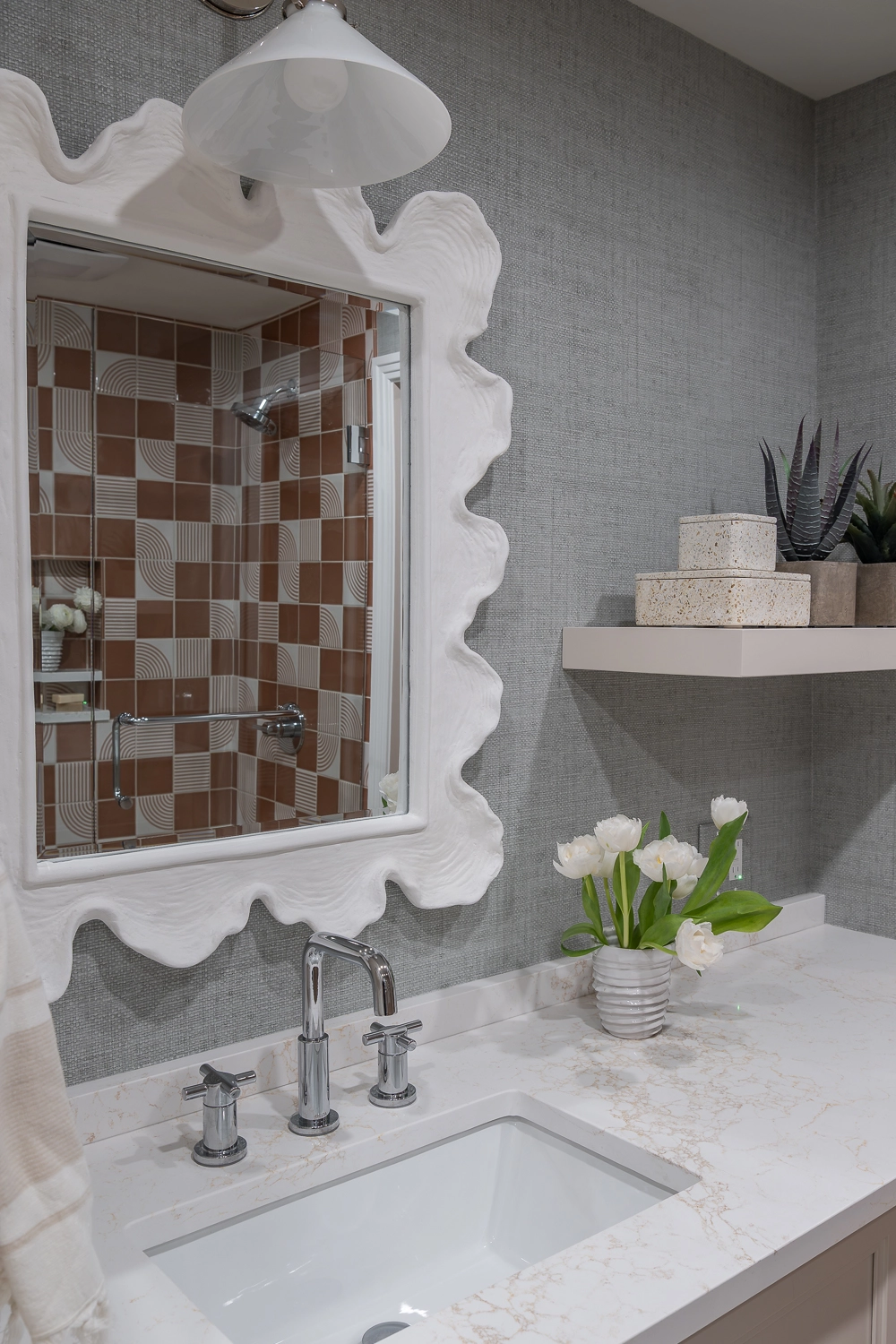 image of vanity in guest bathroom with large white wavey mirror and floating shelving with accessories