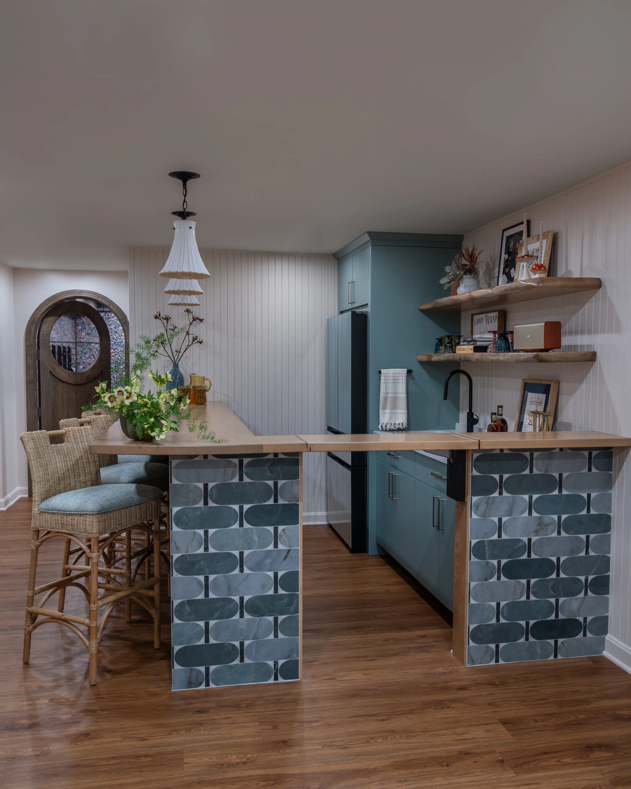 Lower Level playful bar with rattan coutnertsools and decorative penants with white shade and stained wood countertop
